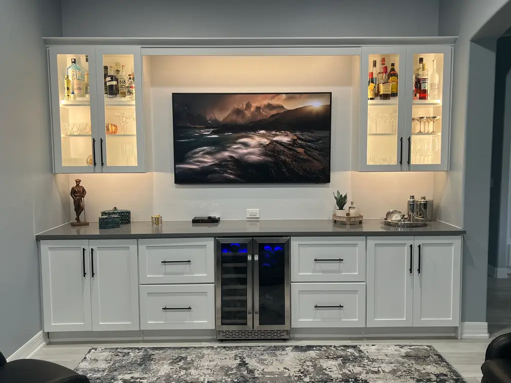 White bar wall with lit glass-front cabinets, beverage cooler and quartz counter