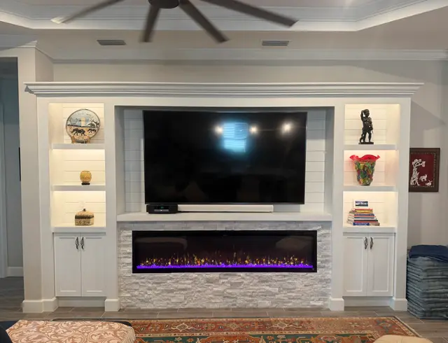 White crown-molded built-in with lit shiplap shelves and a stacked-stone linear electric fireplace