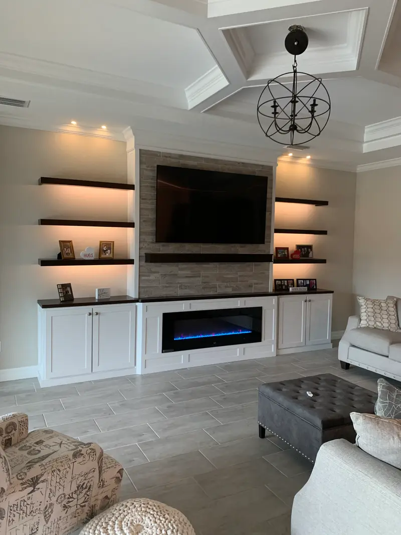 Stone media wall with dark floating shelves and white base cabinets