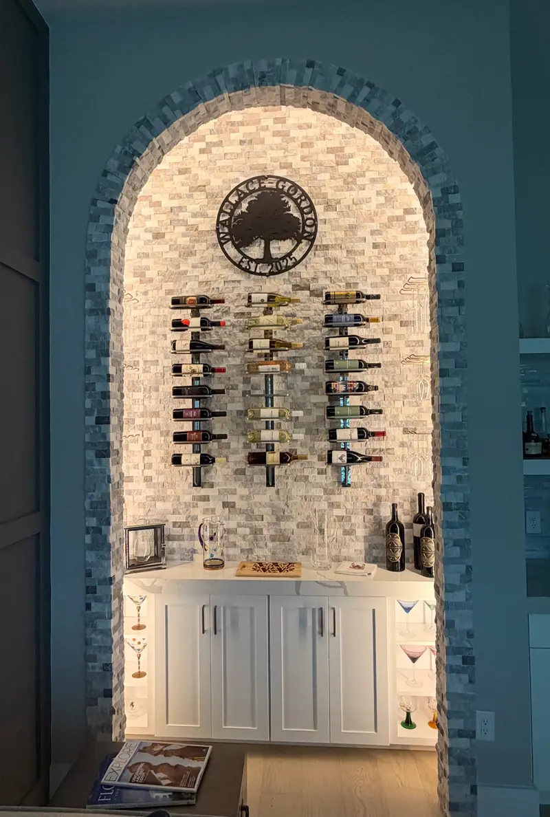Lit stone-mosaic archway wine nook with floating bottles and white cabinetry