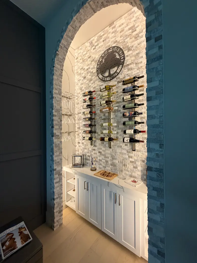 Side view of a stone-mosaic wine nook with glass holders and a white counter